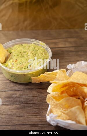 Tortilla Chip in Guacamole neben einem Sack Chips Stockfoto