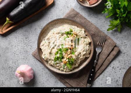 Baba Ganoush Vorspeise aus gebackener Aubergine mit frischer Petersilie, Walnüssen, Knoblauch und Olivenöl auf grauem Hintergrund. Arabische und libanesische Küche. Ausblick Stockfoto