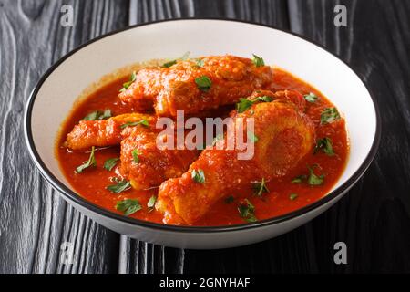 Authentisches Ayam Masak Merah Rezept aus Hühnerstücken, die in einer würzigen Tomatensauce in einer Schüssel auf dem Tisch in der Nähe übergossen werden. Horizontal Stockfoto