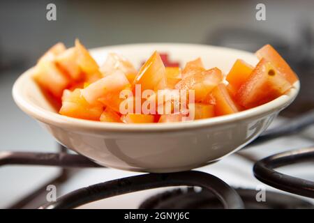 Gewürfelte Tomaten in einer weißen Schüssel auf einem weißen Herd Stockfoto