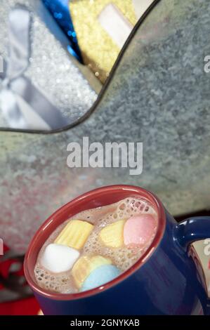 Blau-roter Becher mit bunten Marshmallows neben einem Blechschlitten gefüllt mit Silber, Blau und Gold präsentiert im Hintergrund Stockfoto
