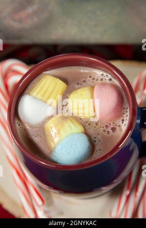 Blauer und roter Becher mit bunten Marshmallows auf einer Holzfläche mit Zuckerstöcken, neben einem Zinnhintergrund Stockfoto