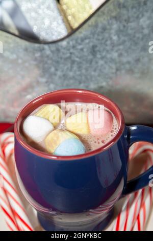 Blauer und roter Becher mit bunten Marshmallows auf einer Holzfläche mit Zuckerstöcken, neben einem Zinnhintergrund Stockfoto