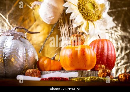 Kleine orange Kürbisse, kleine rote Kürbis, kleine orange Glitter Kürbisse, ein großer silberner Kürbis, rote, gelbe und orange Glitter Blätter, und getrocknete Sonne Stockfoto