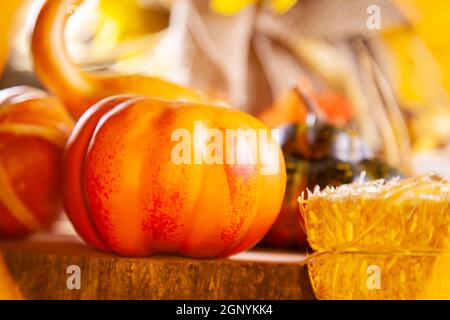 Kleiner orangefarbener Kürbis auf einer hölzernen Plattform neben einem kleinen Heuballen mit goldenem Ton Stockfoto