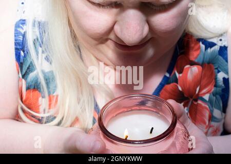 Albino Frau genießt den Duft einer brennenden pfirsichfarbenen Kerze Stockfoto