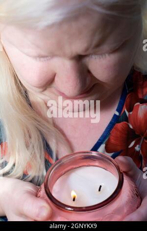 Albino Frau genießt den Duft einer brennenden pfirsichfarbenen Kerze Stockfoto