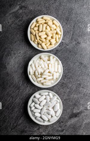 Weiße medizinische Pillen. Pharmazeutische Medikamente Pillen, Tabletten und Kapseln in Schüssel auf schwarzem Tisch. Draufsicht. Stockfoto