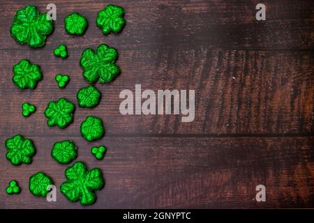 Glitter bedeckt vier Blatt Clovers für Saint Pattys Day Füllung Die Hälfte des Rahmens auf einem Holzhintergrund Stockfoto