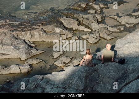 Felsige Küste Siziliens ein paar Touristen sitzen auf den Lavafelsen am Meer in Cefalù Stockfoto