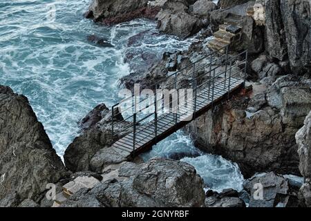 Felsküste Siziliens in Cefalù kleine Brücke auf den Lavasteinen, die vom rauen Meer getroffen werden Stockfoto