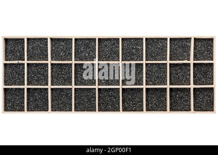 Schwarzer dekorativer Sand in einer rechteckigen Holzkiste mit quadratischen Fächern verteilt. Stockfoto