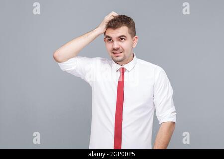 Porträt eines jungen hübschen nachdenklichen verwirrt Mann in weißem Hemd und Krawatte stehen Kratzen seinen Kopf und Denken. Indoor isoliert auf grauem Hintergrund. Stockfoto