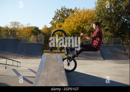 Der junge bmx-Biker springt im Skatepark an die Wand. Extremer Fahrradsport, gefährlicher Radtrick, Straßenreiten, Radfahren im Sommerpark Stockfoto