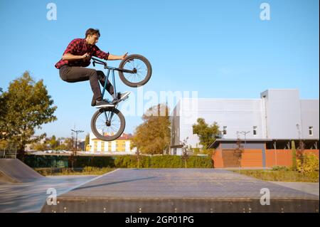 Männlicher bmx-Biker springt auf die Rampe, Teenager trainiert im Skatepark. Extreme Fahrradsport, gefährliche Radsport-Bewegung, Risiko Straßenreiten, Radfahren im Sommer Stockfoto