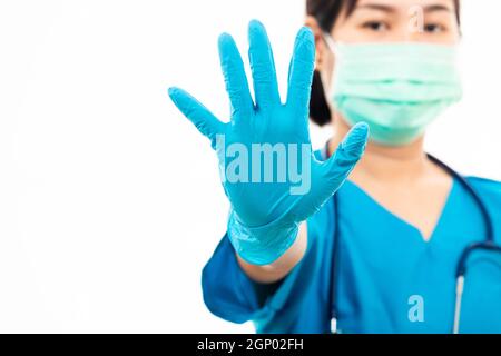 Weibliche Krankenschwester mit Stethoskop setzt Gummihandschuhe und trägt medizinische Gesichtsmaske, Frau Arzt in blauen Uniform zeigen Hand Stop-Zeichen, Studio erschossen isola Stockfoto