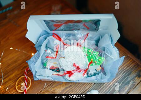 Weihnachtsgeschenk für Kinder mit Lebkuchen in der Glasur. Schachtel mit Keksen, Dekorationen und Girlande auf Holztisch. Festliche Komposition. Stockfoto