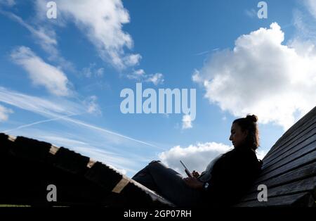 28. September 2021, Baden-Württemberg, Tübingen: Eine Frau sitzt auf einer Holzcouch und schaut in ihr Mobiltelefon. Foto: Marijan Murat/dpa Stockfoto