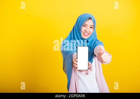 Asiatisch muslimisch arabisch Frau Islam tragen Schleier hijab lustig lächeln sie zeigt leeren Bildschirm smart Handy und Point-Bildschirm, Studio erschossen auf gelb isoliert Stockfoto