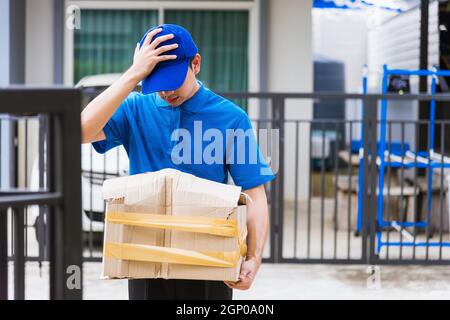 Asiatische junge Lieferung Mann in blauer Uniform er emotional fallen Kurier halten beschädigte Karton ist an der Tür vor Hause gebrochen, Unfall schlechten Transport Stockfoto