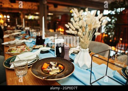 Wunderschön gedeckte Tische mit Essen, Gläsern und Geräten im Restaurant. Stockfoto