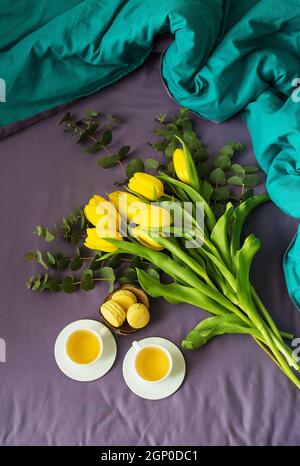 Gelbe Tulpen, Cookies und zwei Tassen Tee im Bett, Nahaufnahme Stockfoto