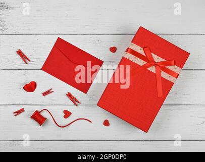 Vorbereitung Valentine Geschenke, rote Box, Herzen, Garn, Wäscheklammern und Notiz in Papierumschlag auf weißem Holztisch Hintergrund, close up flach legen, heben Stockfoto