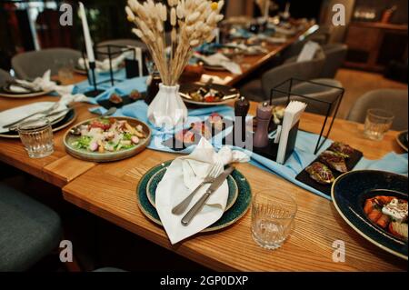 Wunderschön gedeckte Tische mit Essen, Gläsern und Geräten im Restaurant. Stockfoto