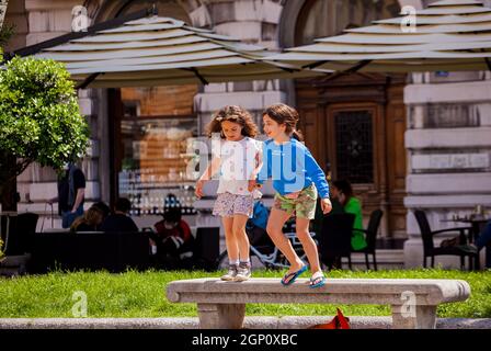 Triest, Italien - Mai 31: Zwei glückliche weibliche Kinder haben am 31. Mai 2021 Spaß daran, von der Bank im Park zu springen Stockfoto