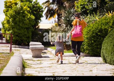 Triest, Italien - Mai 31: Rückansicht einer Mutter mit ihrer kleinen Tochter, die am 31. Mai 2021 im Park spazierenging Stockfoto