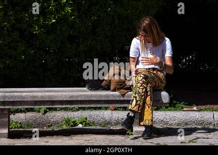 Triest, Italien - Mai 31: Eine junge Frau, die auf der Bank sitzt, schaut sich am 31. Mai 2021 ein Video am Telefon an und schützt den Blick vor der Sonne Stockfoto