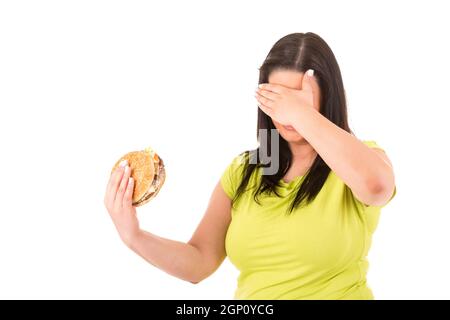 Schöne große Frau, die versucht, zu einem appetitlichen Hamburger widerstehen können, die ihre Ernährung töten würde Stockfoto