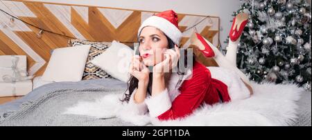 Junge schöne Mädchen in rot Santa Claus suit liegt auf dem Bett und schaut verträumt in die Ferne gegen den Hintergrund der Wohnung dekoriert für Chri Stockfoto