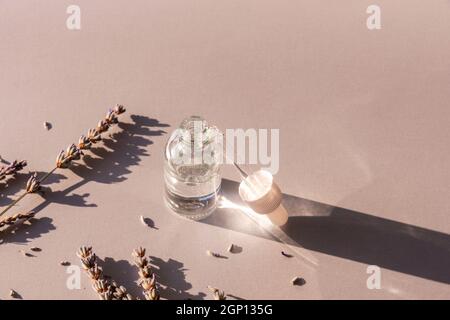 Lavendelblüten und kosmetisches Serum in Glasflasche auf hellgrauem Hintergrund, Draufsicht. Aromatherapie und Naturkosmetik Konzept. Stockfoto