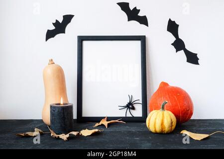 Halloween Feiertagskonzept mit leerem Bilderrahmen, Kürbissen, Kerze, Fledermäusen und Spinne auf schwarz-weißem Hintergrund. Modell. Stockfoto