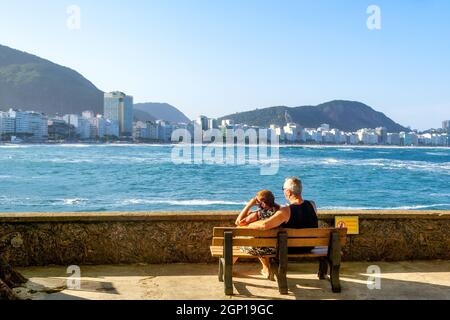 Ein Paar, das auf einer Bank sitzt und vom Strand der Copaba in Rio de Janeiro, Brasilien, aus die Landschaft blickt. Dieser Ort ist eine berühmte Touristenattraktion i Stockfoto