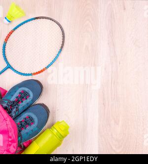 Zwei blaue Damen-Sneakers und eine Flasche im pinken Rucksack, Badminton-Schläger und Federball auf weißer Holzoberfläche Stockfoto