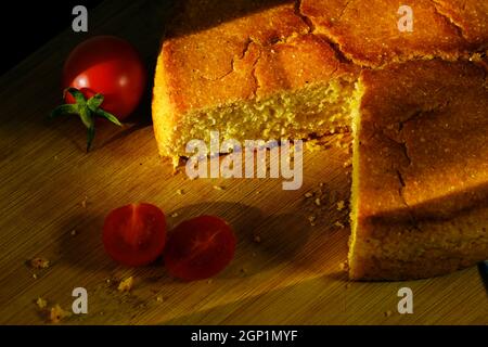 Nahaufnahme von Maisbrot und Kirschtomaten auf einem Holzbrett mit kreativen harten Schatten Stockfoto