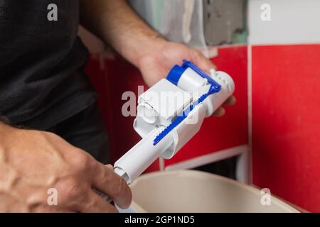 Austausch von Teilen des Toilettentanks. Ein Mann in orangefarbenen Handschuhen repariert den Abfluss des Toilettenbehälters Stockfoto