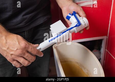 Austausch von Teilen des Toilettentanks. Ein Mann in orangefarbenen Handschuhen repariert den Abfluss des Toilettenbehälters Stockfoto