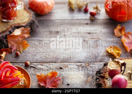 Halloween Essen Stillleben abstrakter Hintergrund mit Kürbissen, Äpfeln, Kuchen, Gummiwürmer, Totenkopf-Rotgetränk und Kerzen Stockfoto