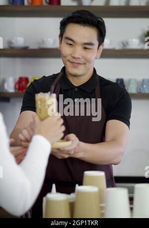 Barista in Schürze serviert Eiskaffee für die Gäste. Morgendliche Atmosphäre in einem Café. Stockfoto