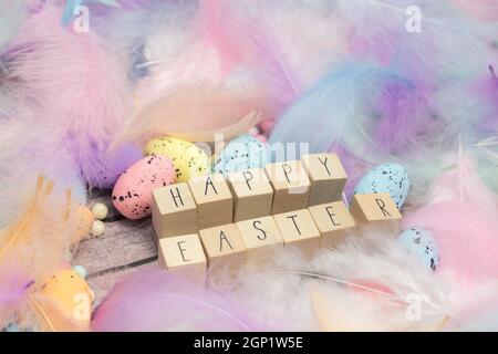 Frohe Ostern geschrieben mit Holzwürfeln umgeben von schönen pastellfarbenen dekorativen Federn und Eiern, April, Ostern, Religion, Frühlingskonzept Stockfoto
