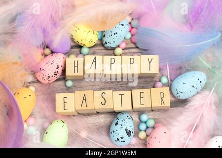Frohe Ostern geschrieben mit Holzwürfeln umgeben von schönen pastellfarbenen dekorativen Federn und Eiern, April, Ostern, Religion, Frühlingskonzept Stockfoto