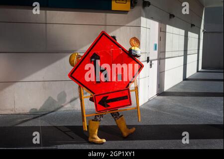 23.09.2021, Singapur, Republik Singapur, Asien - Ein Arbeiter trägt Ausrüstung mit Straßenschildern und Warnleuchten im Stadtzentrum. Stockfoto