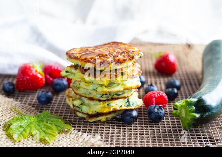 Frische Stapel von köstlichen hausgemachten Zucchini Pfannkuchen mit Honig Ahornsirup, Sommerfrüchte, Zucchini und Ahornblatt auf Küchengrill gekrönt. Nahaufnahme. Stockfoto