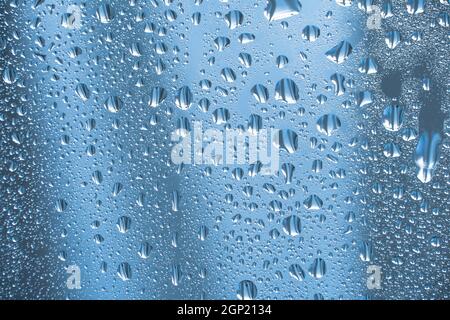 Regentropfen auf dem Glas bei Regenwetter.die glitzernde, glänzende Wasseroberfläche auf dem Glas.Wassertropfen in Form von Kugeln oder Kugeln.Blaue Regentropfen bac Stockfoto