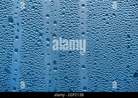 Regentropfen auf dem Glas bei Regenwetter.die glitzernde, glänzende Wasseroberfläche auf dem Glas.Wassertropfen in Form von Kugeln oder Kugeln.Blaue Regentropfen bac Stockfoto