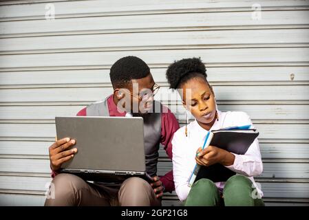 Zwei junge afrikaner diskutieren in einem Café im Freien über das zukünftige Projekt, tragen einen Computer auf dem und ein Notizbuch mit Notizen. Stockfoto