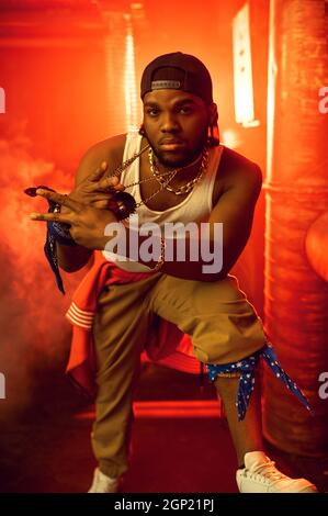 Stilvoller Rapper zeigt seinen Goldschmuck im Studio mit cooler Underground-Dekoration. Hip-Hop-Performer, Breakdance Stockfoto